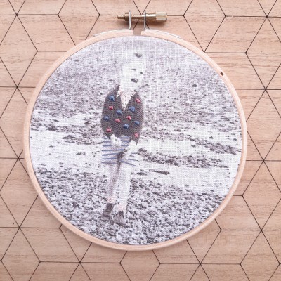 Bastidor de madeira com tecido bordado com imagem a preto e branco e detalhes coloridos