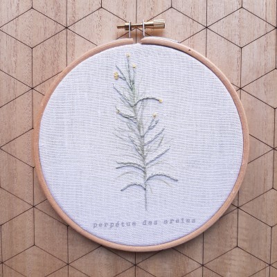 Bordado de ramo verde com flores amarelas em bastidor de madeira sobre superfície de madeira com padrão geométrico