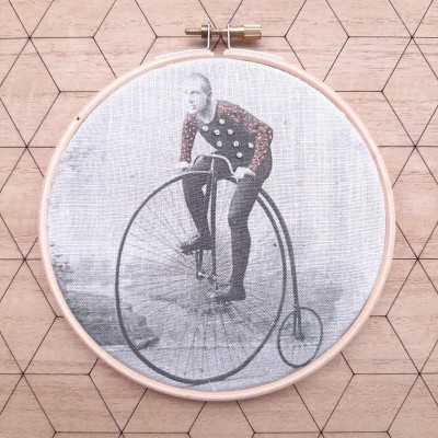 Bastidor de madeira com tecido estampado de homem numa bicicleta antiga sobre fundo de madeira com padrão hexagonal.