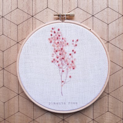 Bastidor de madeira com bordado de flores cor-de-rosa e texto num fundo branco