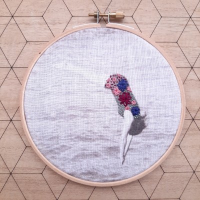 Bordado colorido de ave em tecido branco dentro de aro de madeira