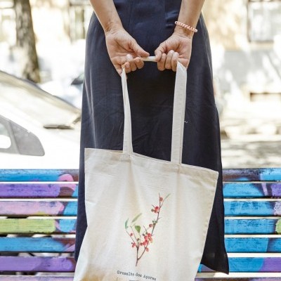 Mulher segurando sacola branca estampada com texto e ramo, sentada em banco colorido.