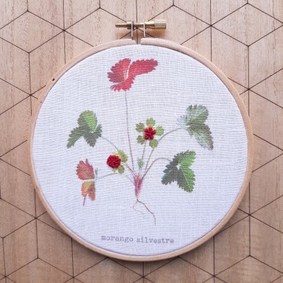 Bordado de morango silvestre em bastidor de madeira sobre fundo geométrico de madeira clara