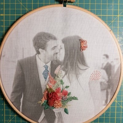 Tecido com imagem de casal e flores bordadas em aro de madeira sobre tapete de corte verde