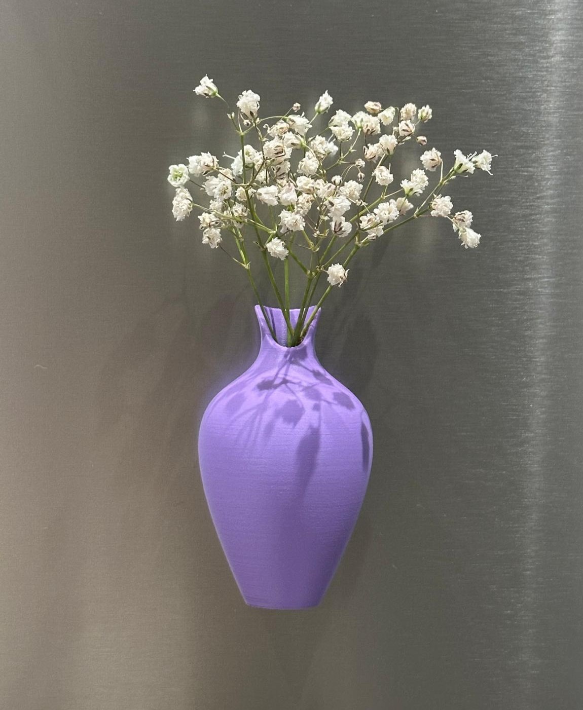 Vaso roxo com flores brancas contra fundo metálico cinza