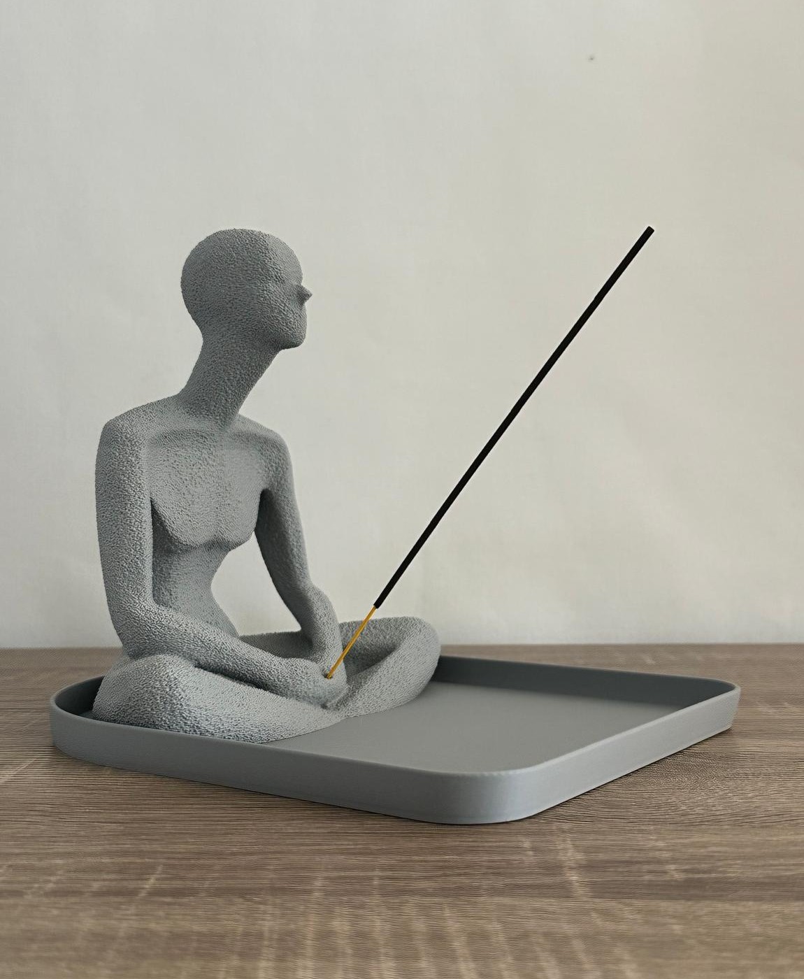 Escultura cinzenta texturizada de figura humana numa posição sentada segurando um incensário com incenso