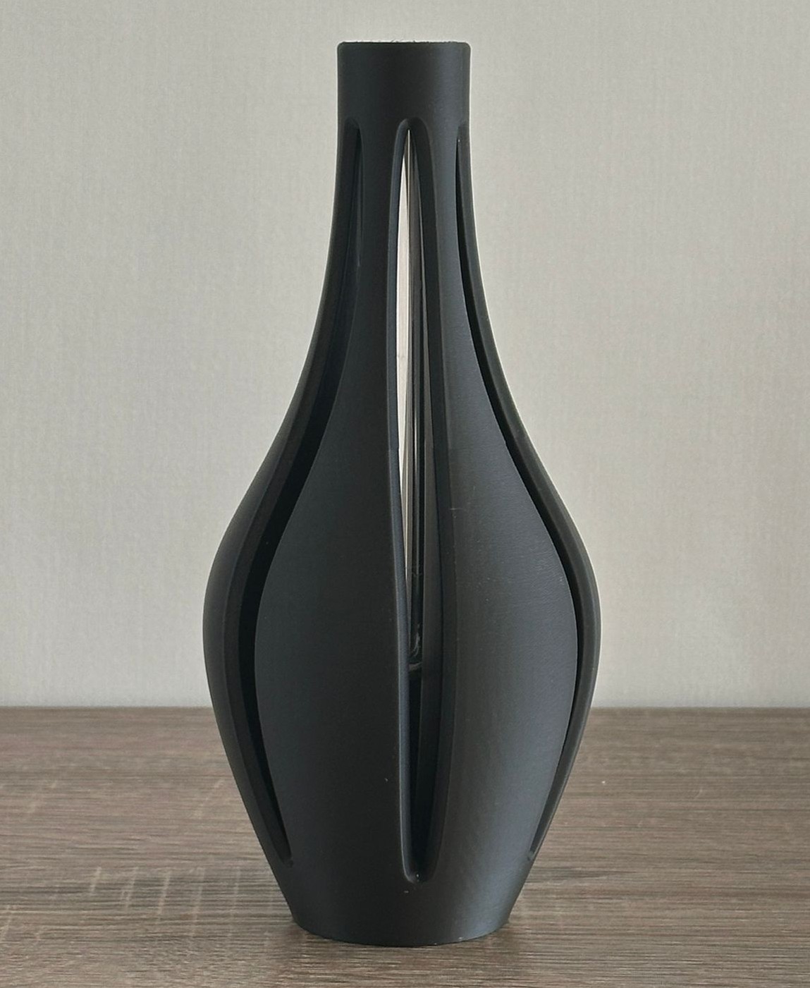 vaso decorativo preto fosco com recortes verticais sobre superfície de madeira