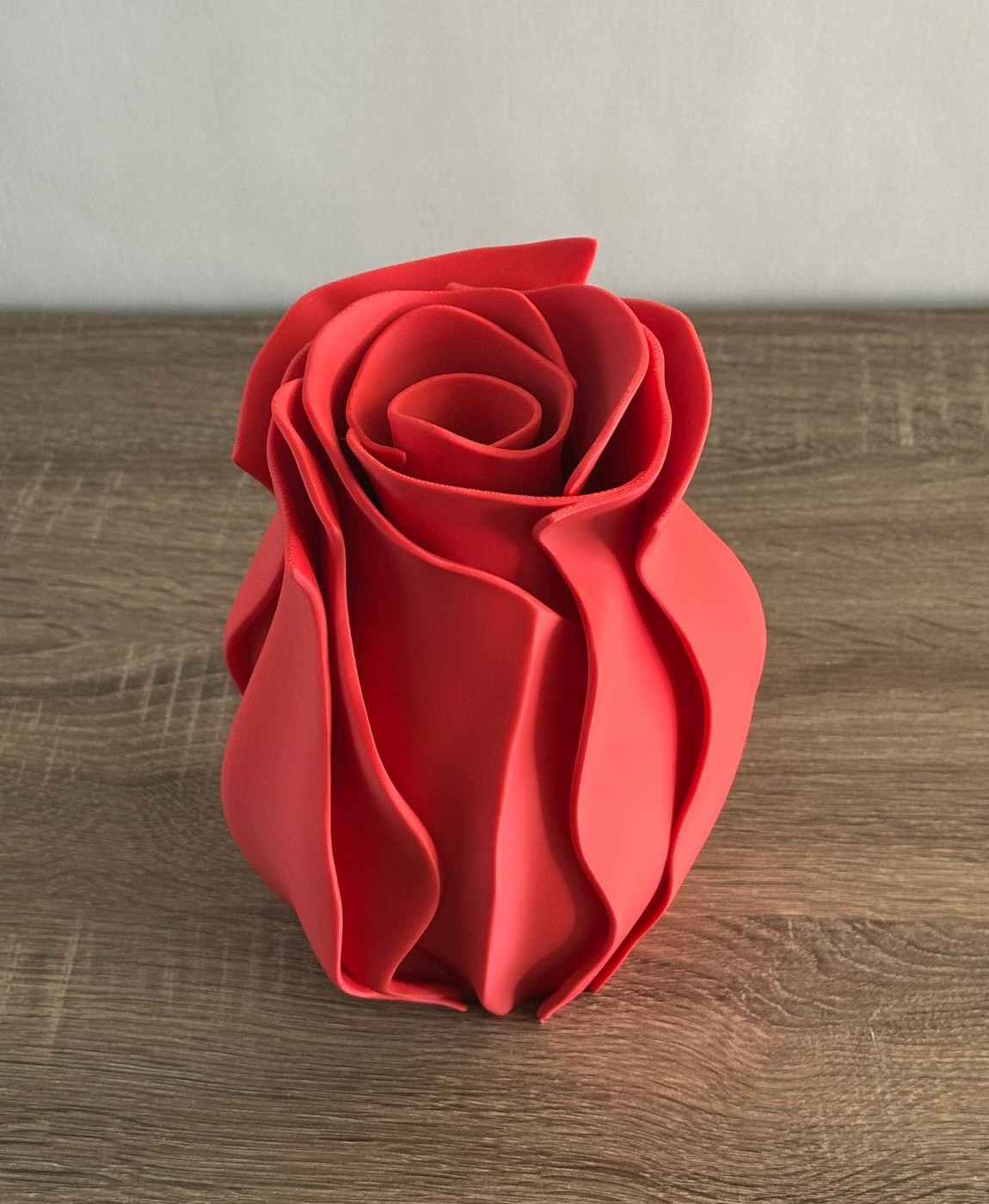 Vaso vermelho em forma de rosa sobre mesa de madeira clara