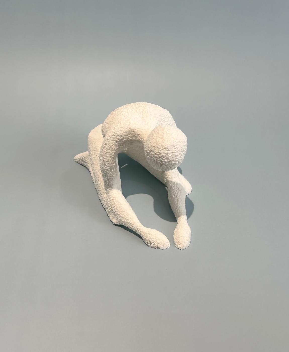 Estatueta branca texturizada de figura humana ajoelhada