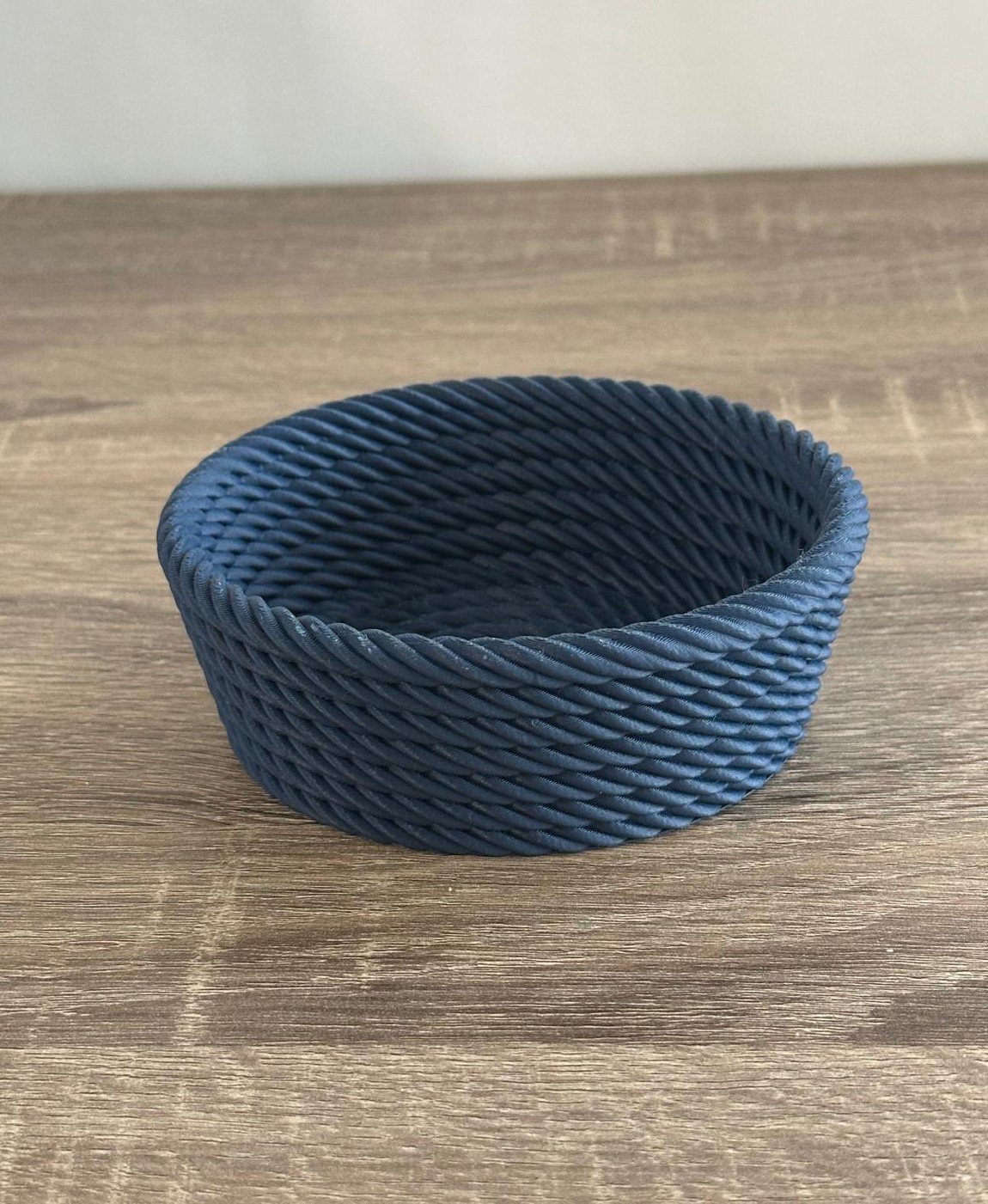 Cesto redondo azul de material sintético trançado sobre superfície de madeira