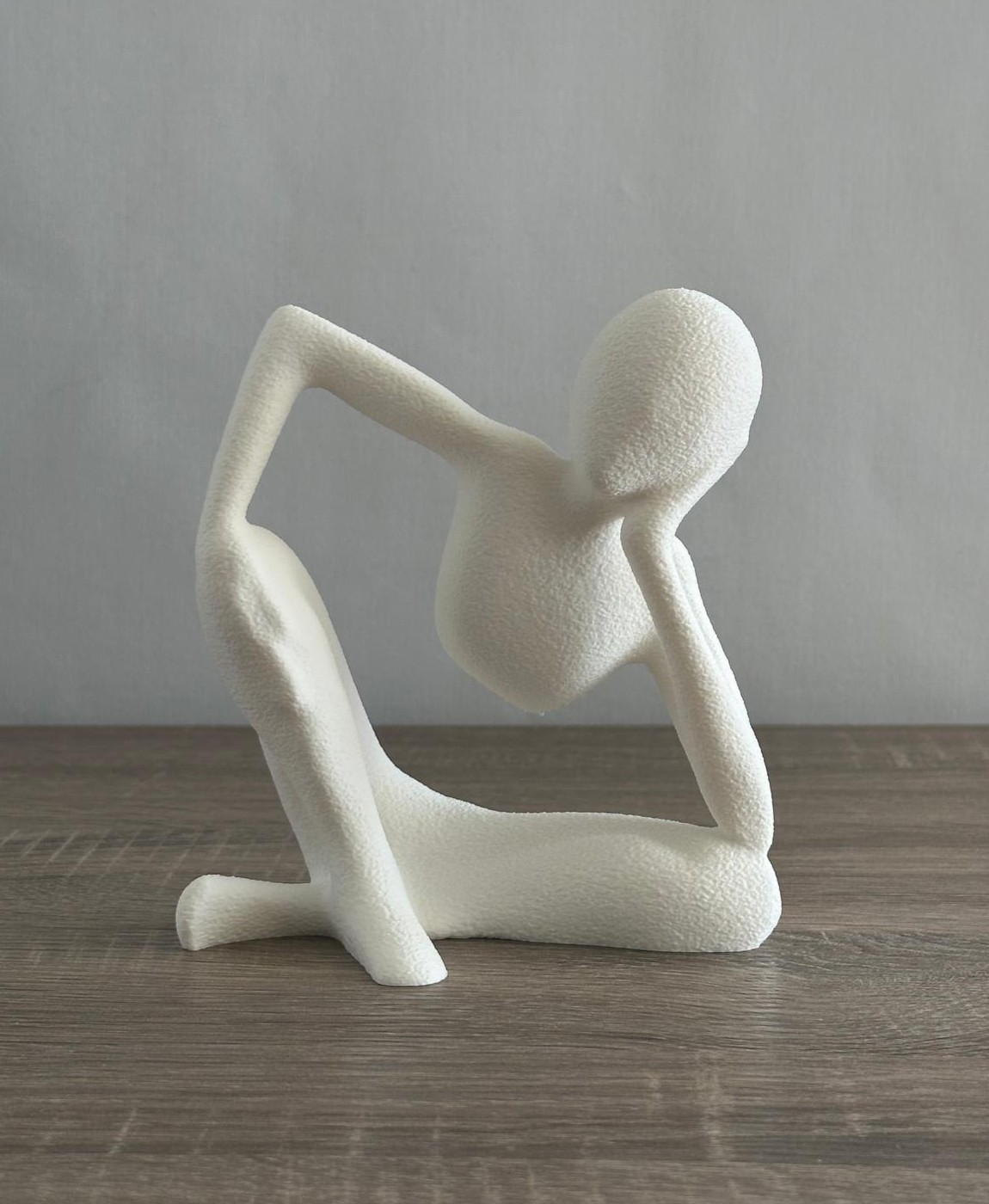 Escultura abstrata branca de figura humana sentada em madeira clara