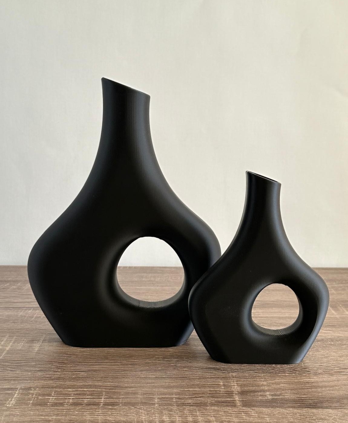 Dois vasos decorativos pretos com recorte circular colocados sobre mesa de madeira