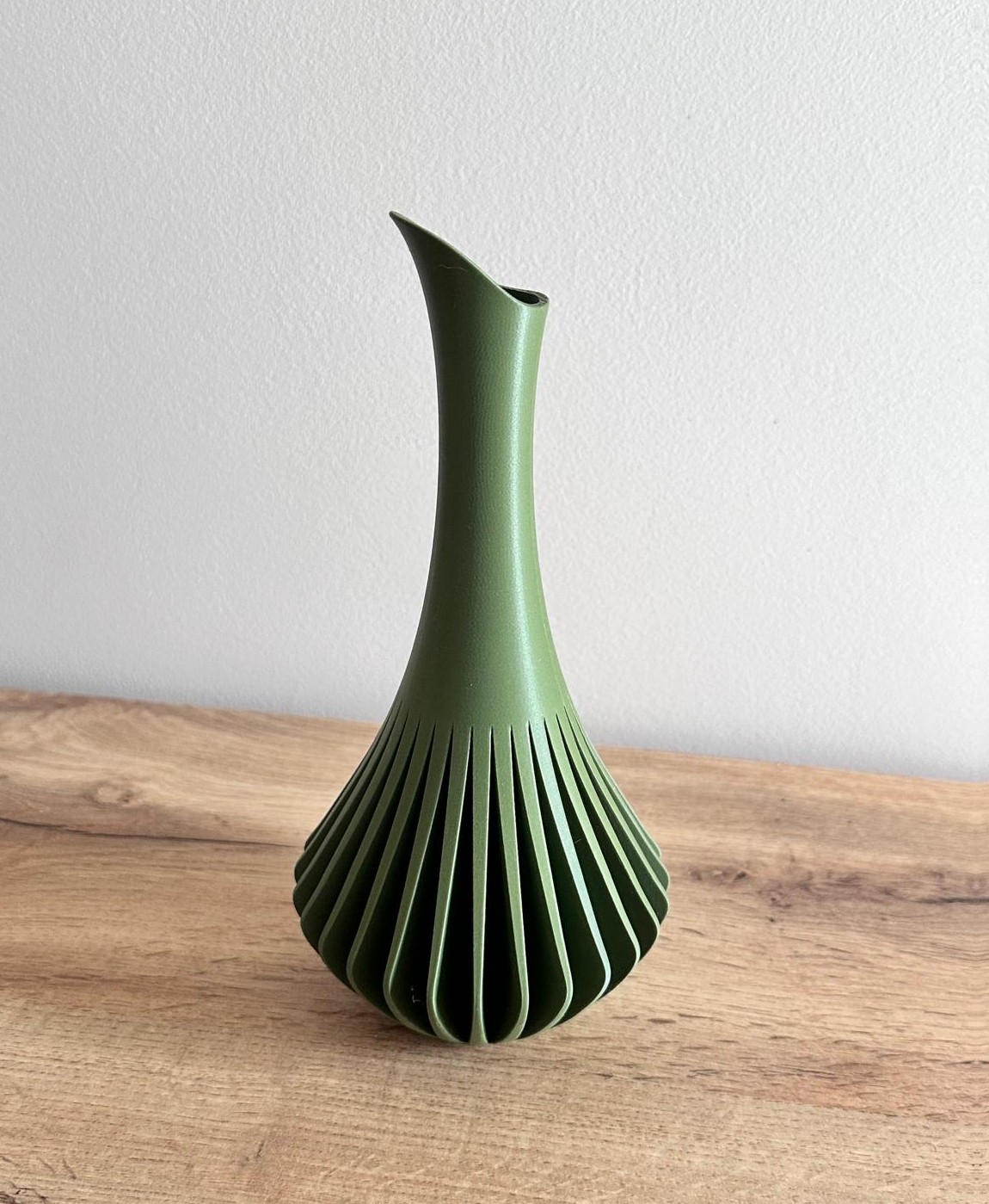 Jarro decorativo verde com recortes verticais ondulados sobre mesa de madeira