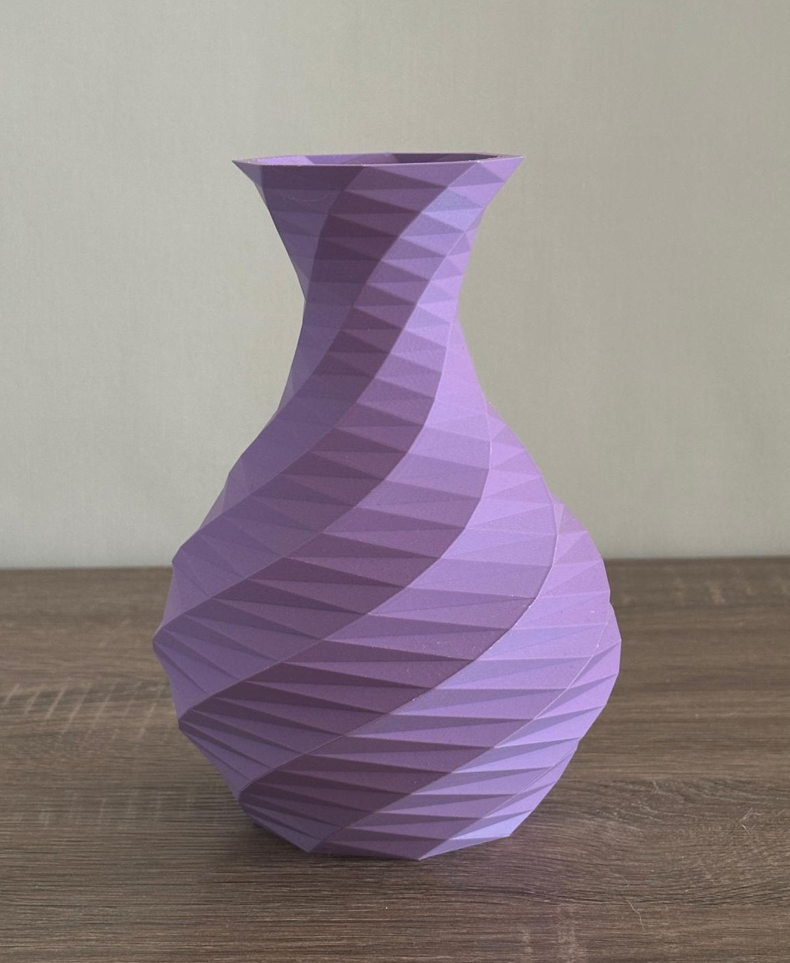 Vaso lilás com textura geométrica espiral em superfície de madeira.