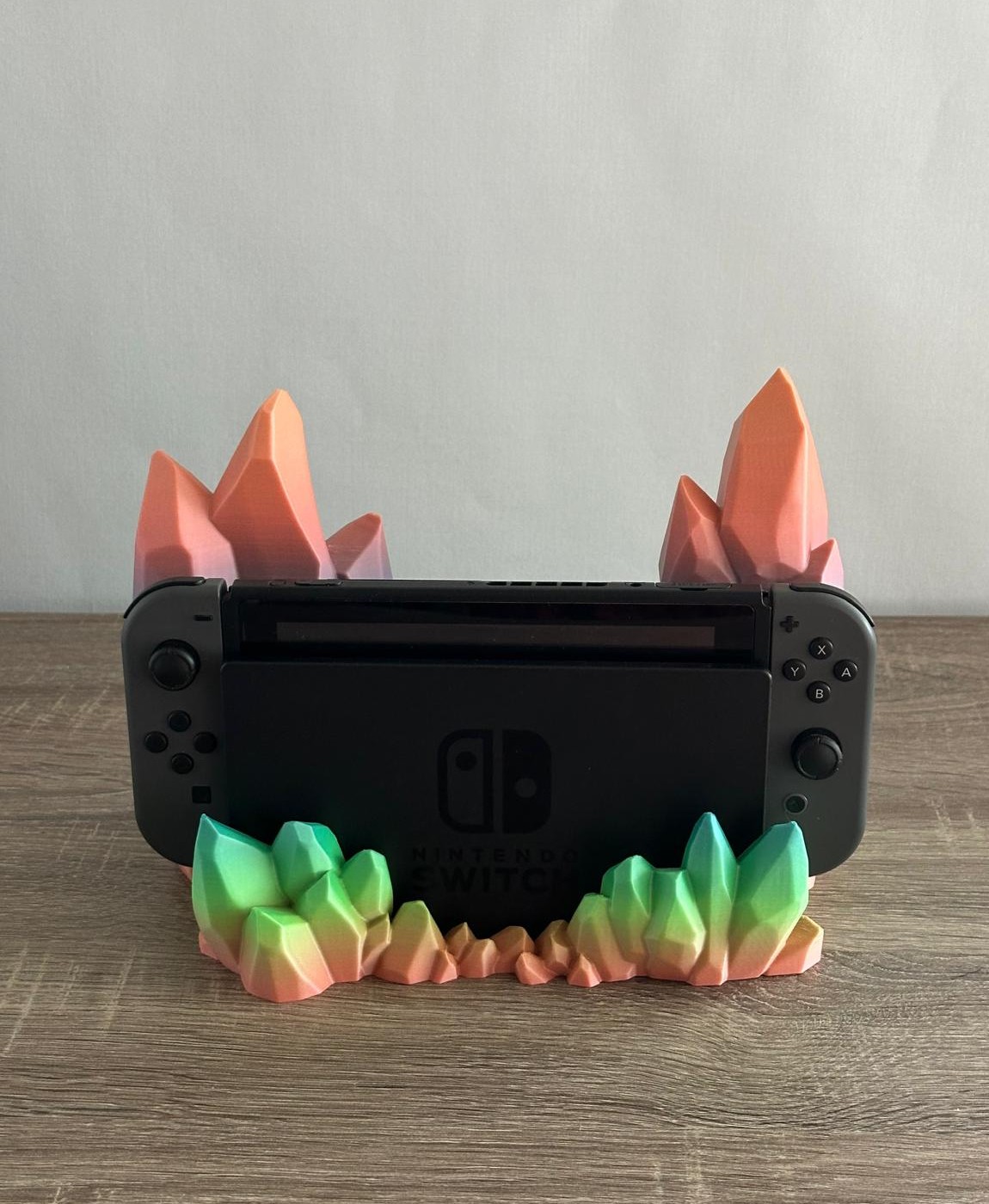 Nintendo Switch preto num suporte com decoração de cristais coloridos em verde, rosa e laranja numa mesa de madeira clara