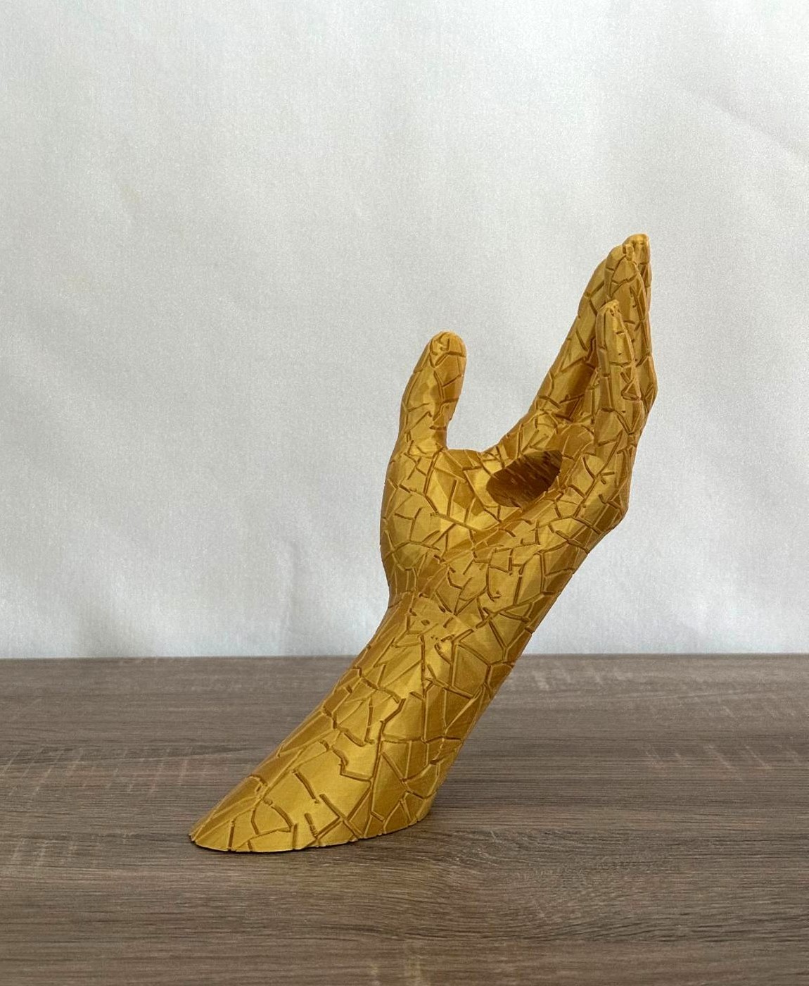 Escultura dourada de mão com padrão geométrico em fundo branco.