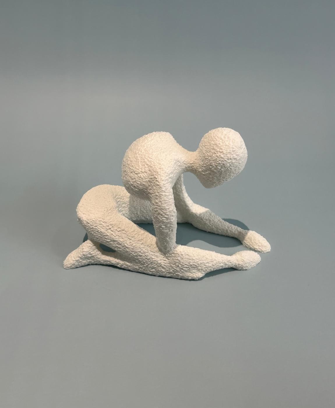 Figurinha decorativa branca com textura rugosa de uma pessoa sentada inclinado para frente