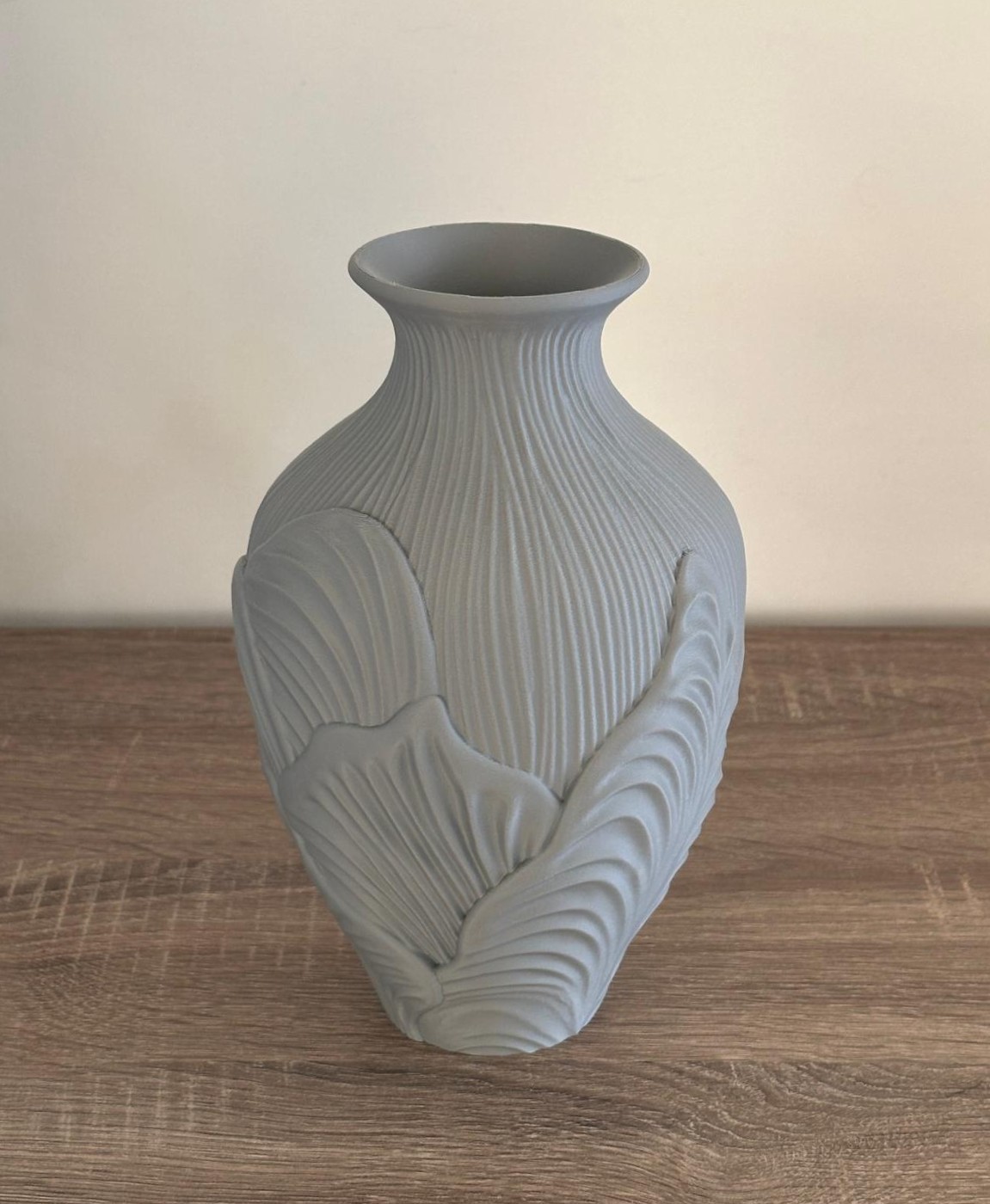 Vaso cinzento em cerâmica com padrão de folhas em relevo sobre mesa de madeira.