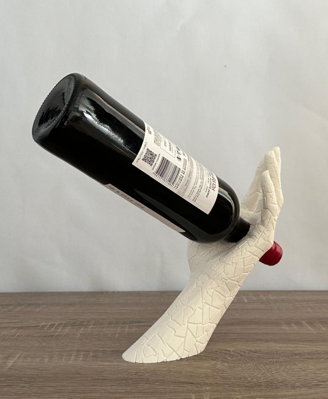 Suporte de mão branco com garrafa escura em superfície de madeira
