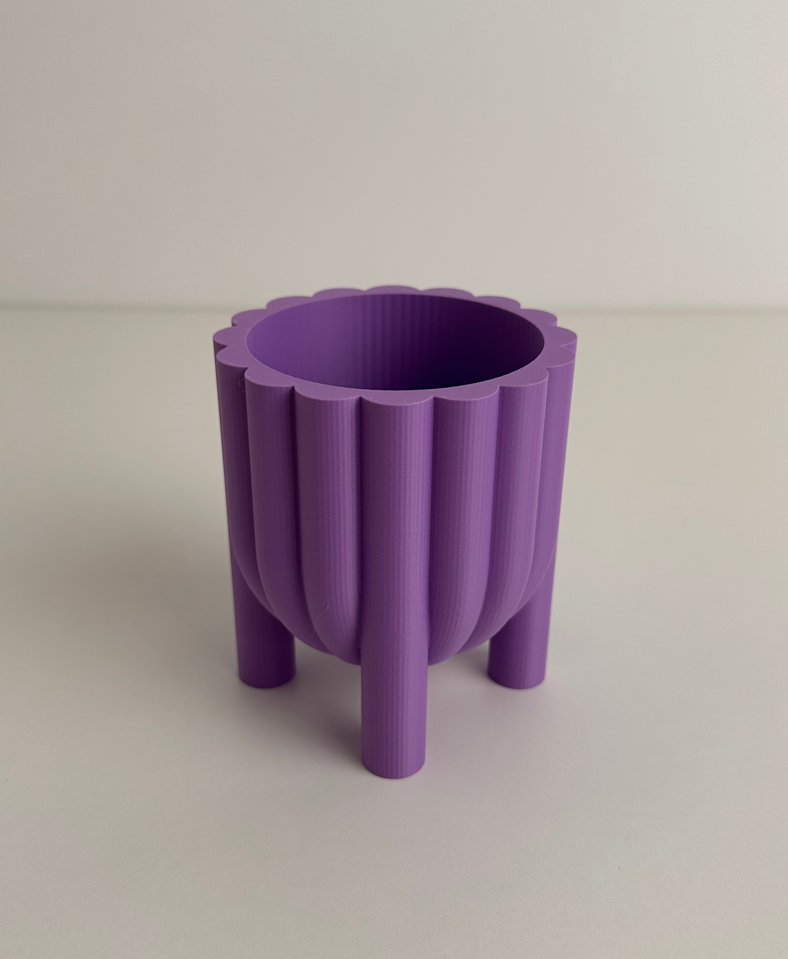Vaso roxo de plástico com design canelado e três pés em fundo branco