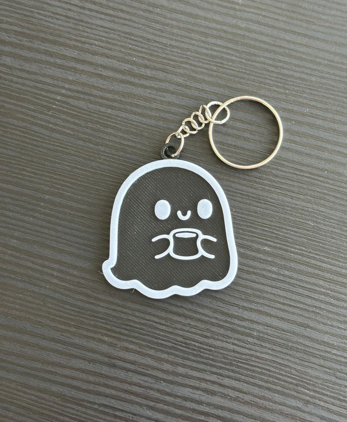 Chaveiro de fantasma transparente com contorno branco e argola dourada sobre superfície cinzenta texturizada