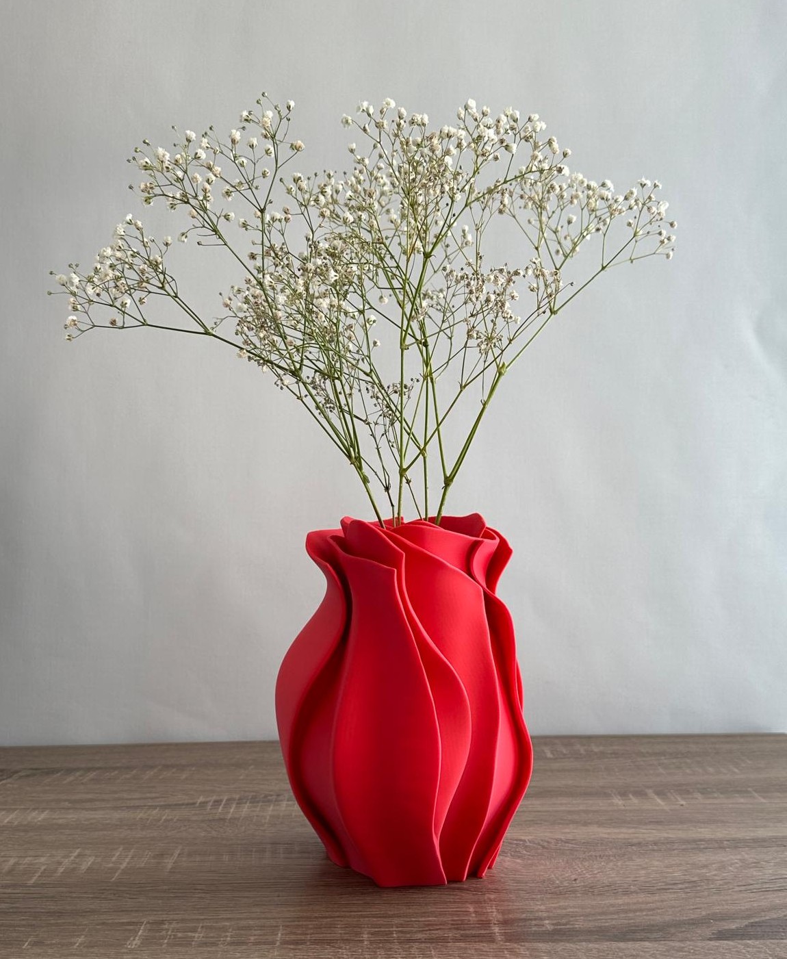 Vaso vermelho ondulado com flores brancas sobre mesa de madeira
