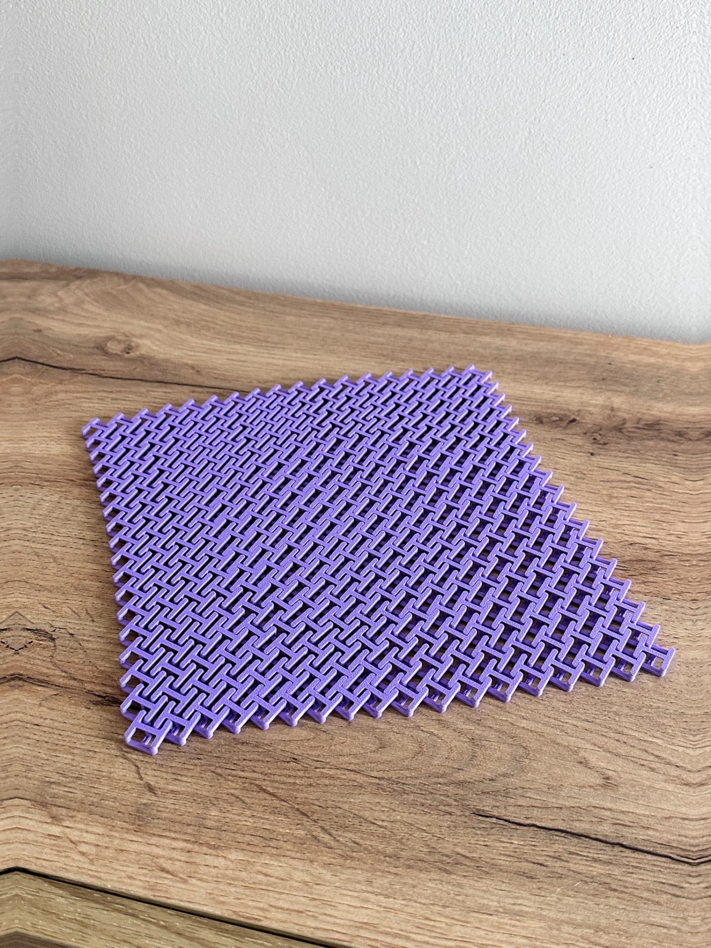 Base quadrada roxa de plástico com padrão entrelaçado em cima de mesa de madeira clara