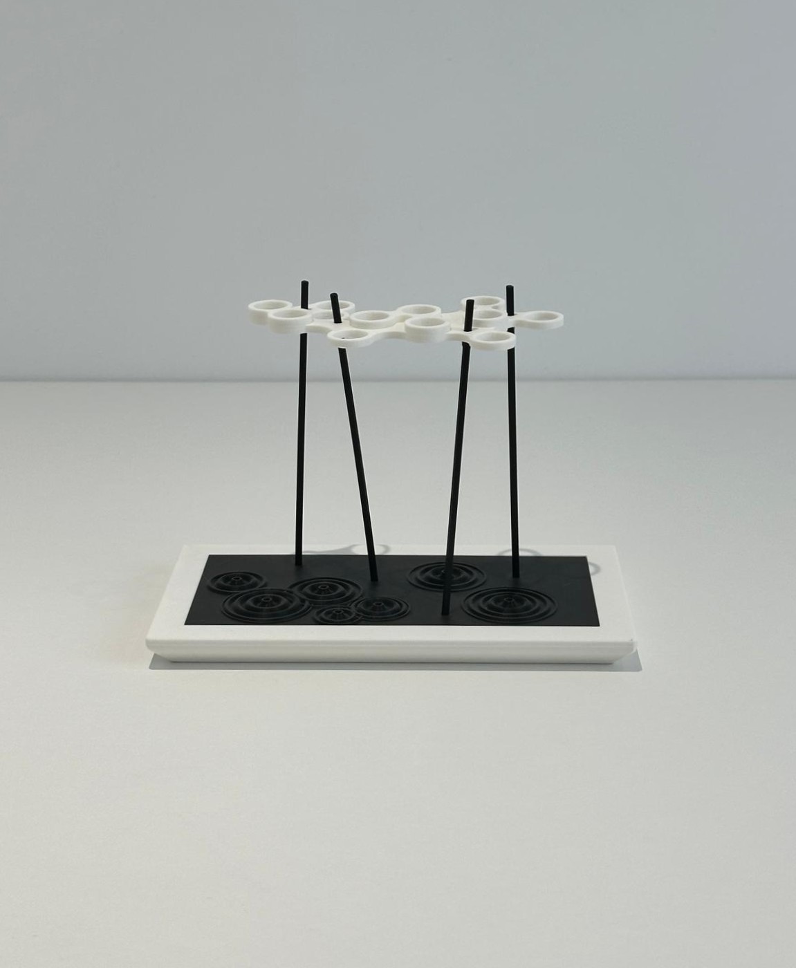 Suporte minimalista para copos com estrutura em metal preto e argolas brancas sobre base retangular