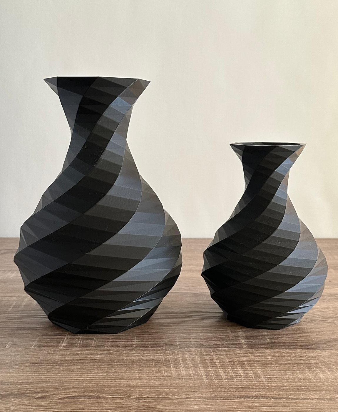 Dois vasos decorativos pretos e cinza com padrão espiral sobre mesa de madeira.