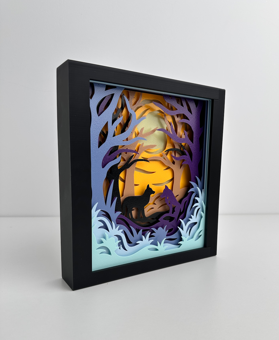 Quadro decorativo em papel com árvores e lobos em moldura preta.