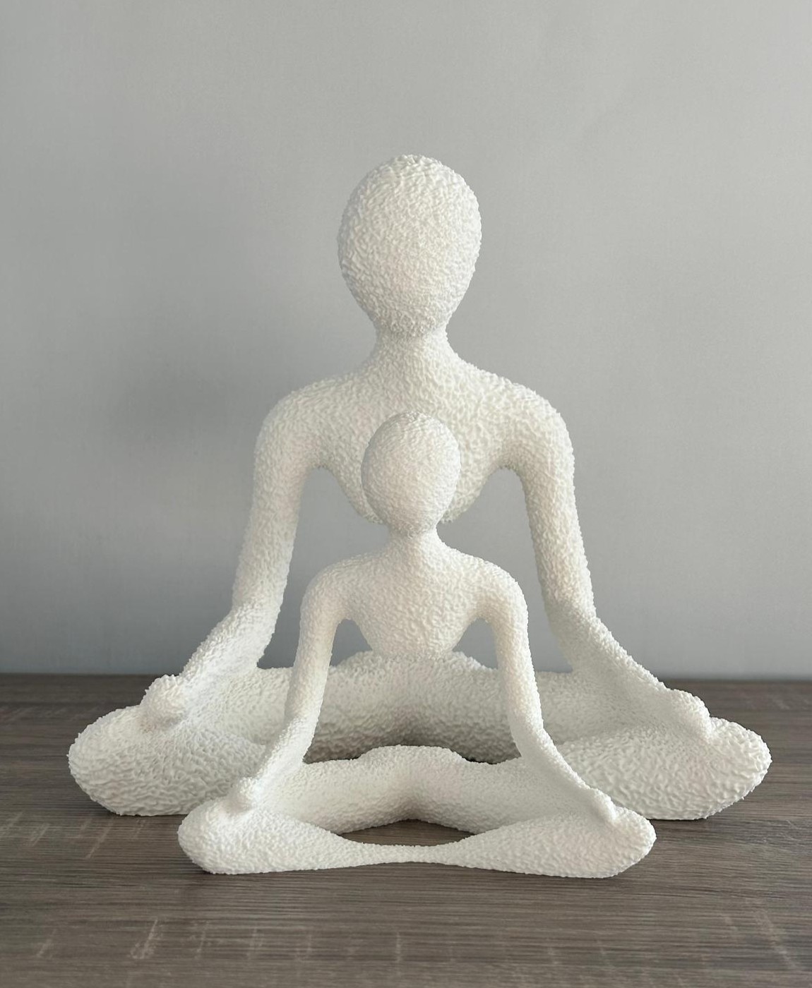 Escultura decorativa branca em textura áspera com duas figuras abstratas sentadas em pose de meditação