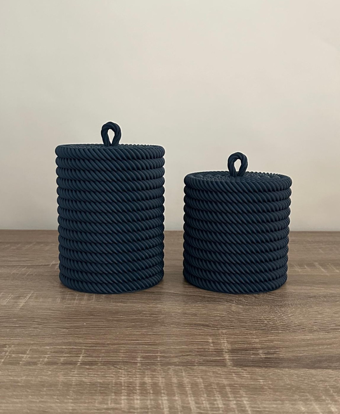 Dois objetos cilíndricos de corda azul com alça no topo sobre mesa de madeira.