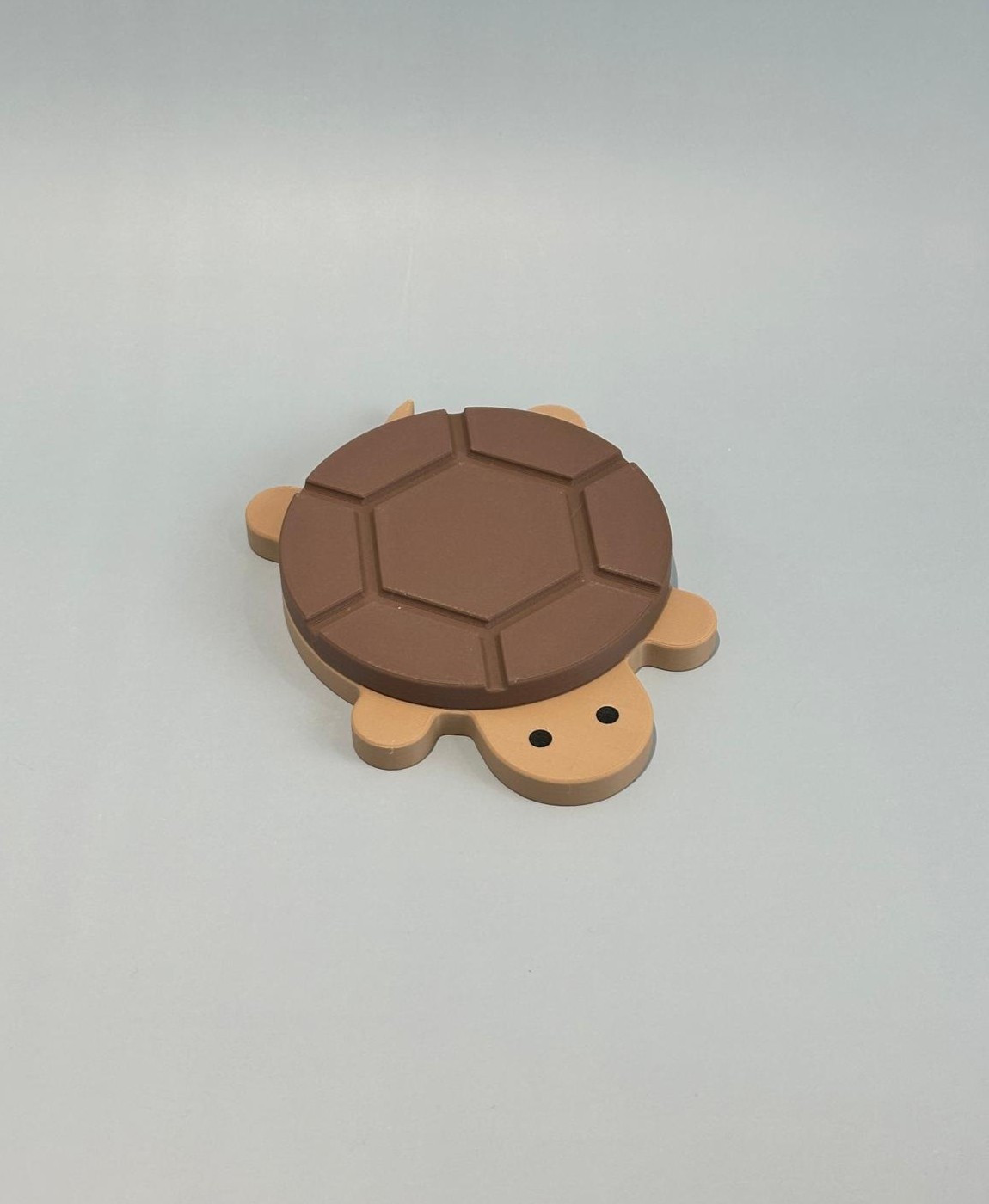 Produto em forma de tartaruga castanho e bege sobre fundo cinzento