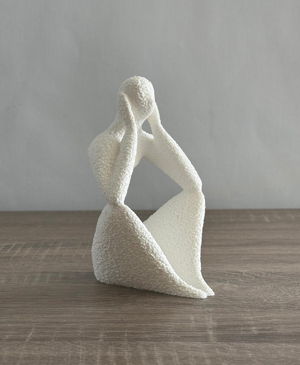 Escultura branca abstrata de figura humana sentada com mãos na cabeça