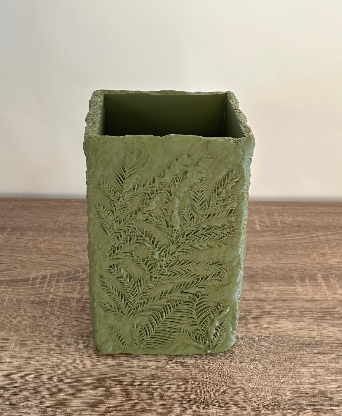 Vaso retangular verde com textura de folhas sobre mesa de madeira