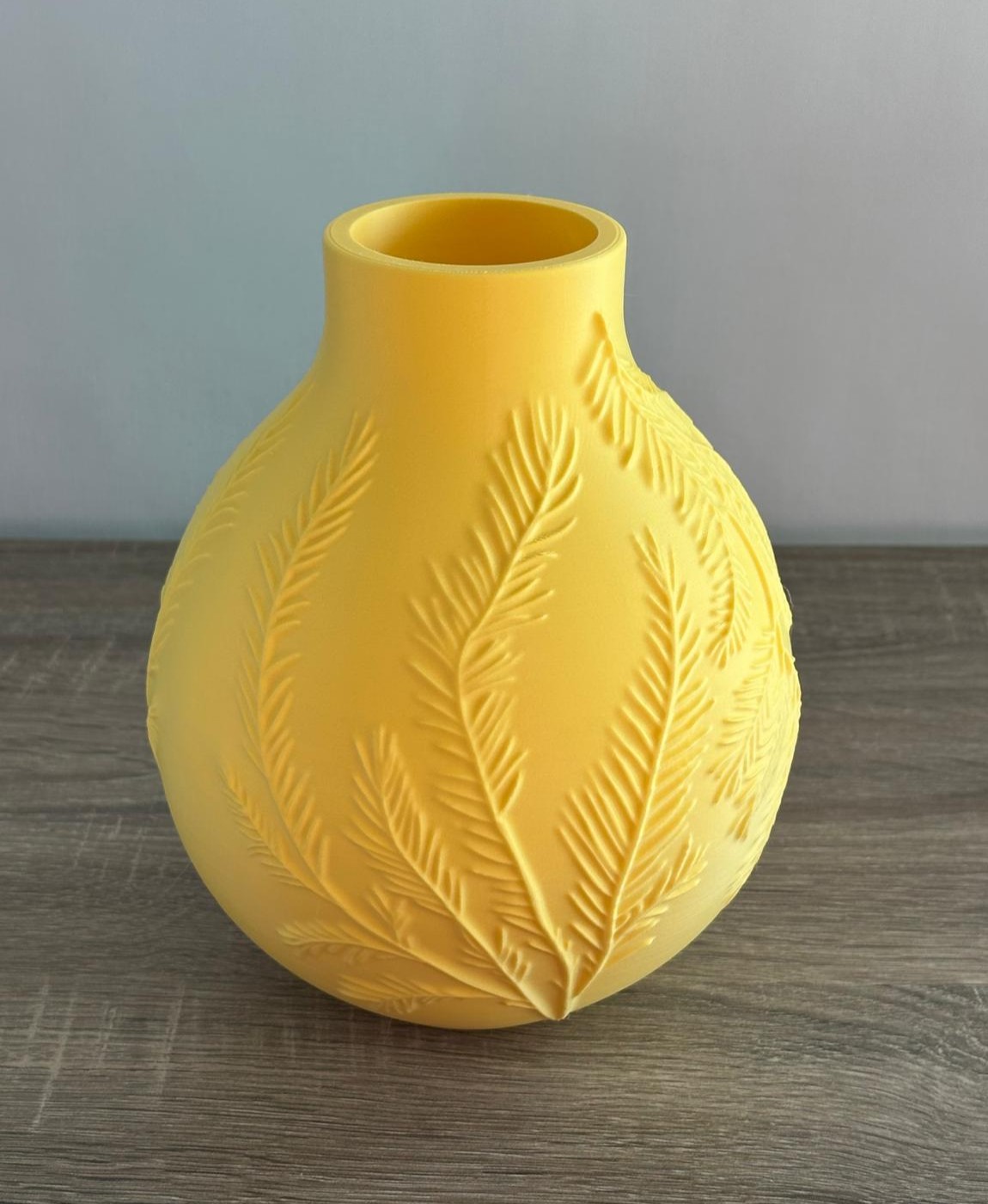 Vaso amarelo redondo com relevo de folhas em superfície de madeira.