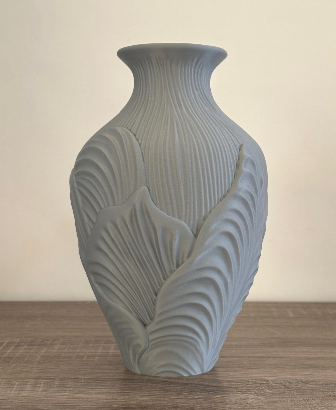 Vaso cinzento texturizado com padrão de folhas em superfície de madeira clara