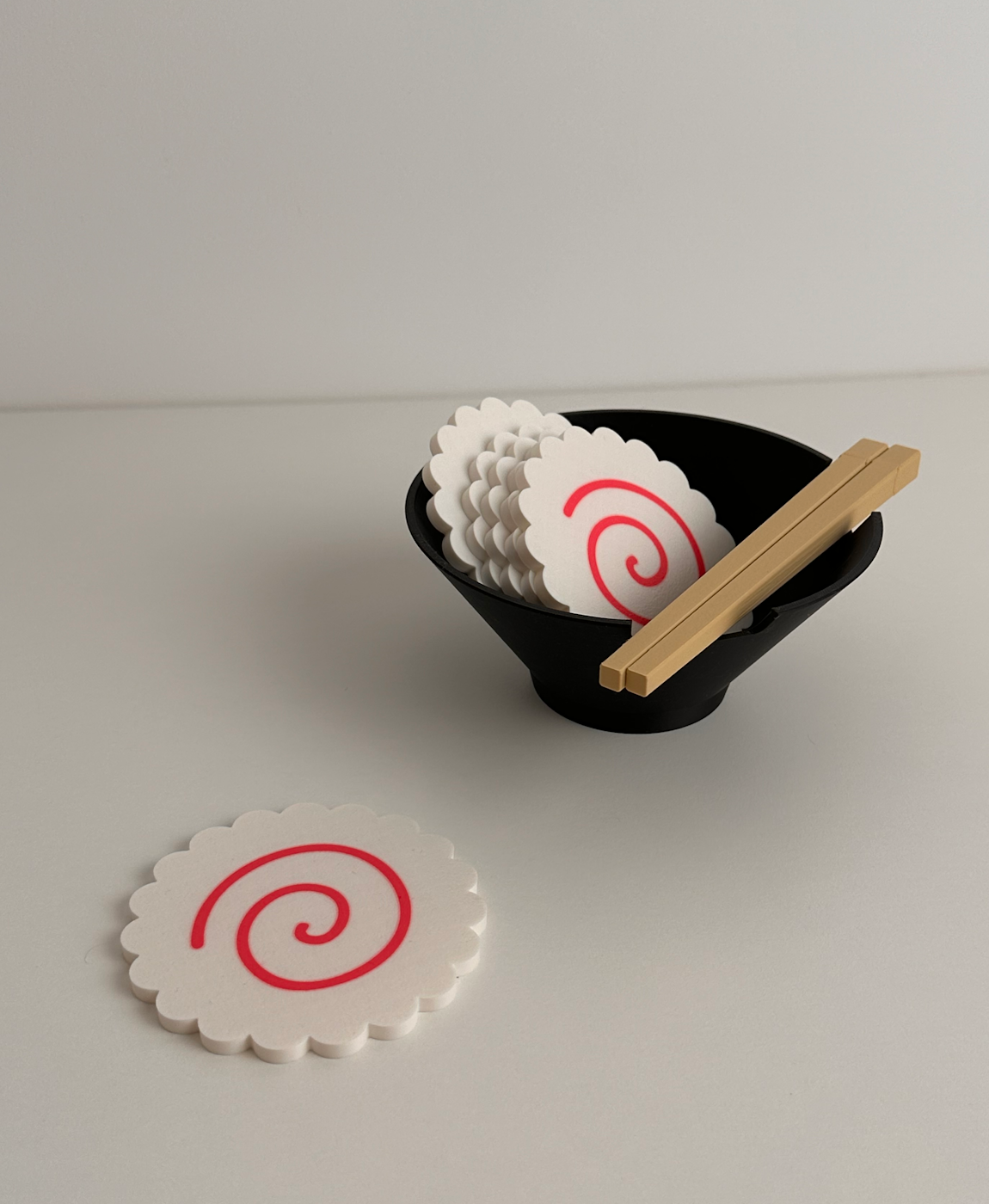 descansos de copos brancos com espiral vermelha numa taça preta com pauzinhos