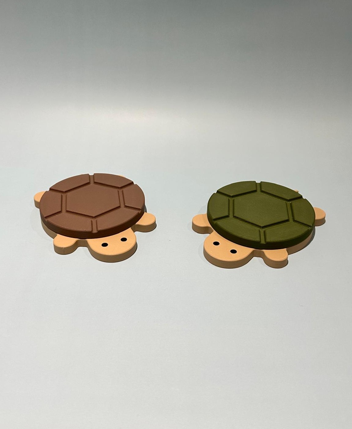 Dois objetos de madeira em forma de tartaruga, um castanho e outro verde, sobre fundo branco