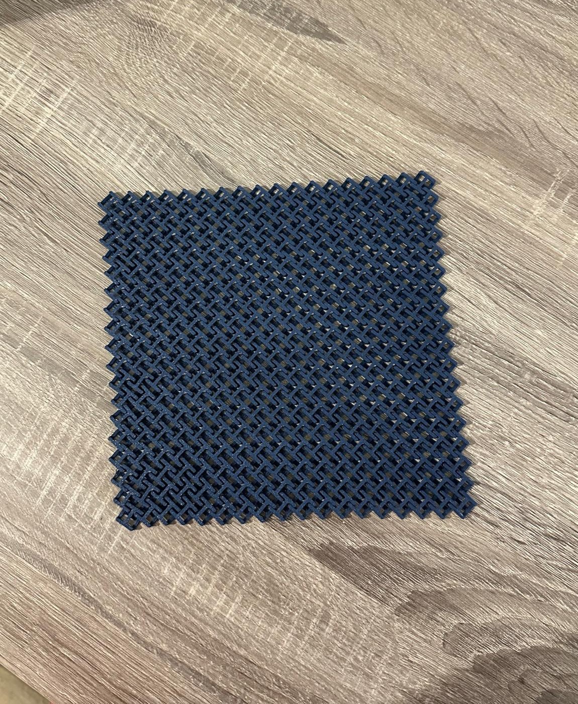 Quadrado de malha plástica azul escura entrelaçada sobre madeira clara