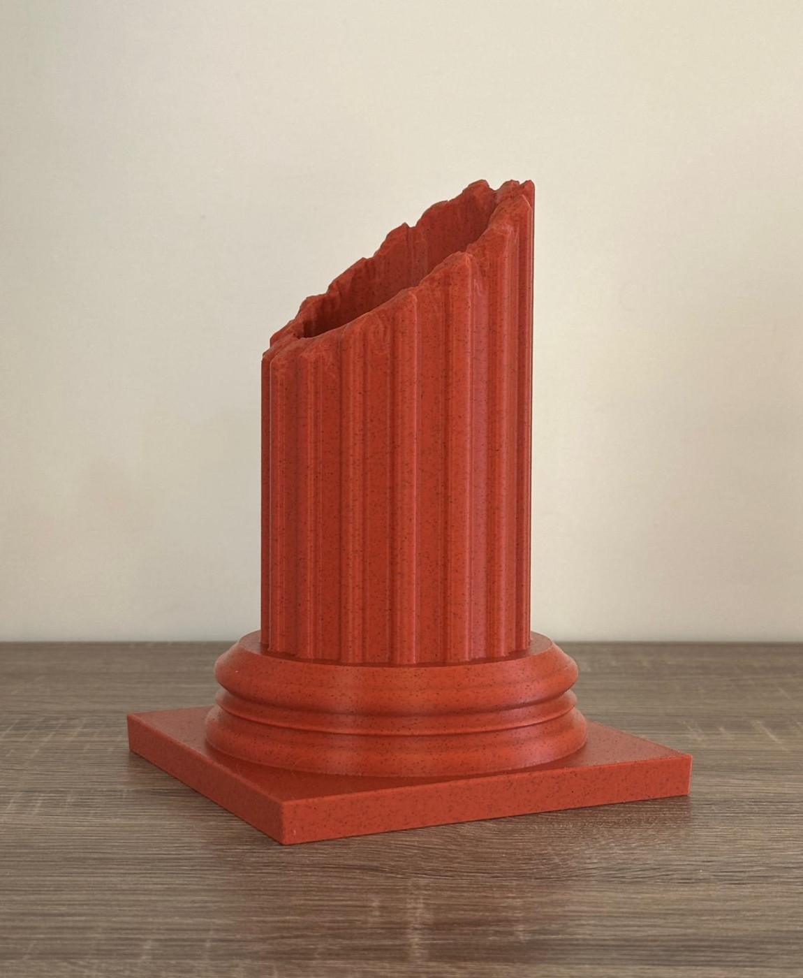 Coluna vermelha decorativa com textura estriada e base quadrada sobre mesa de madeira