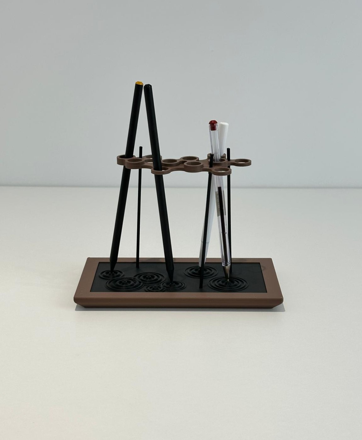 Suporte retangular castanho escuro e preto para pincéis ou canetas numa superfície branca