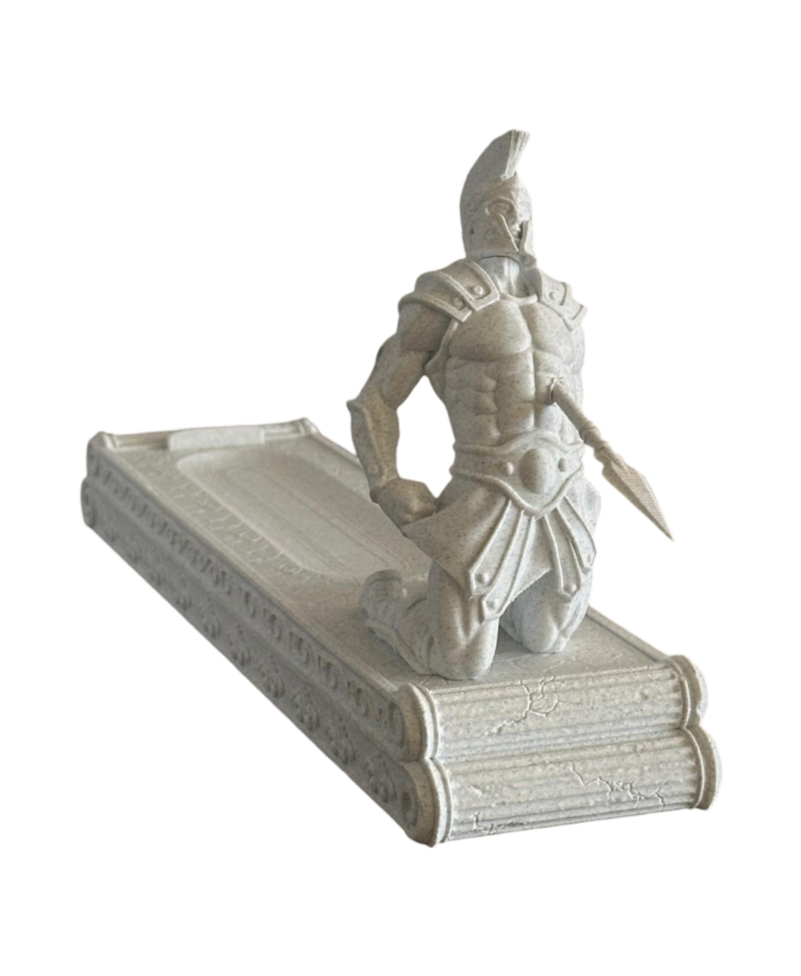 Estatueta de soldado espartano ajoelhado sobre base que parece um livro