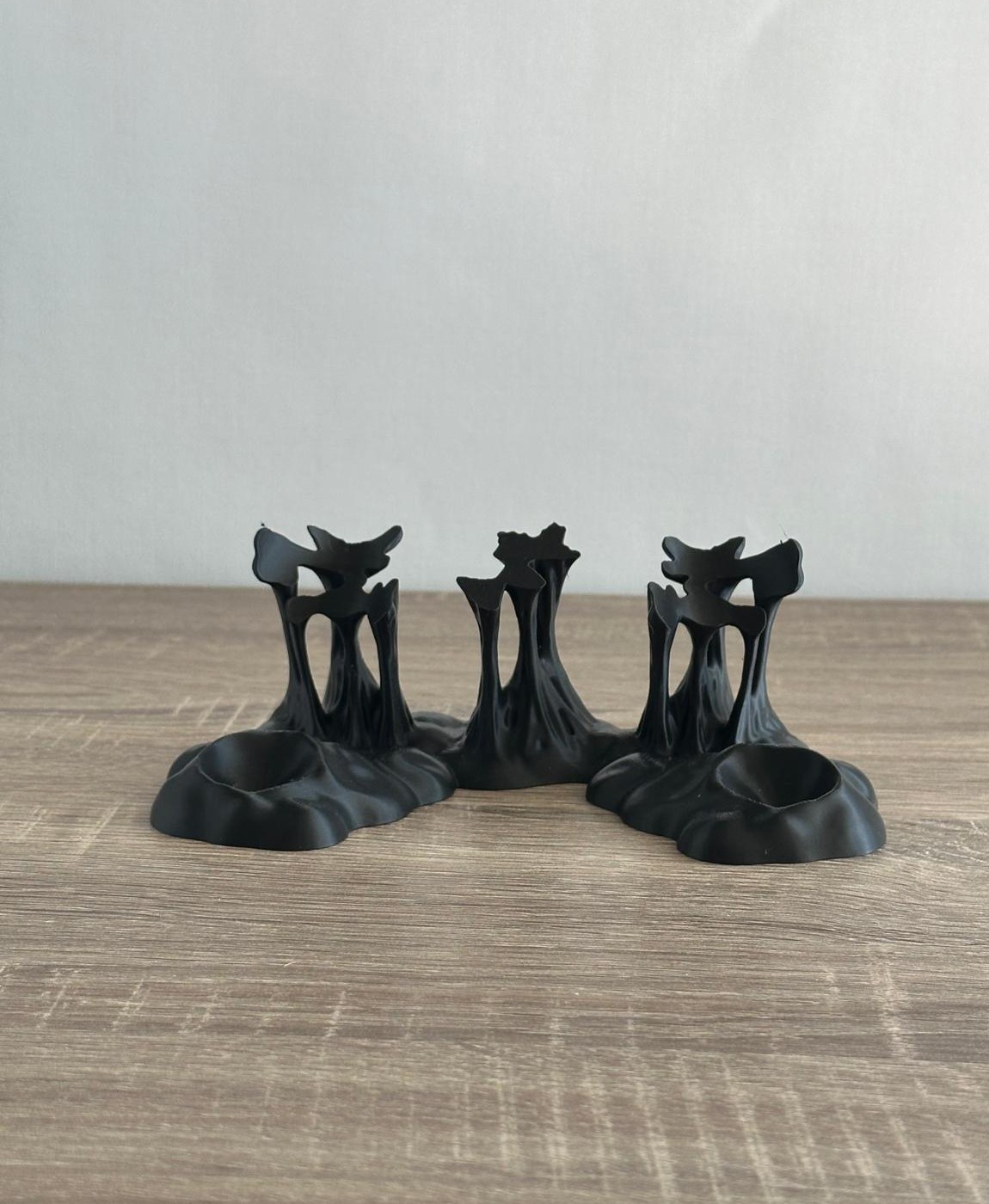 Três castiçais pretos com design orgânico sobre superfície de madeira clara