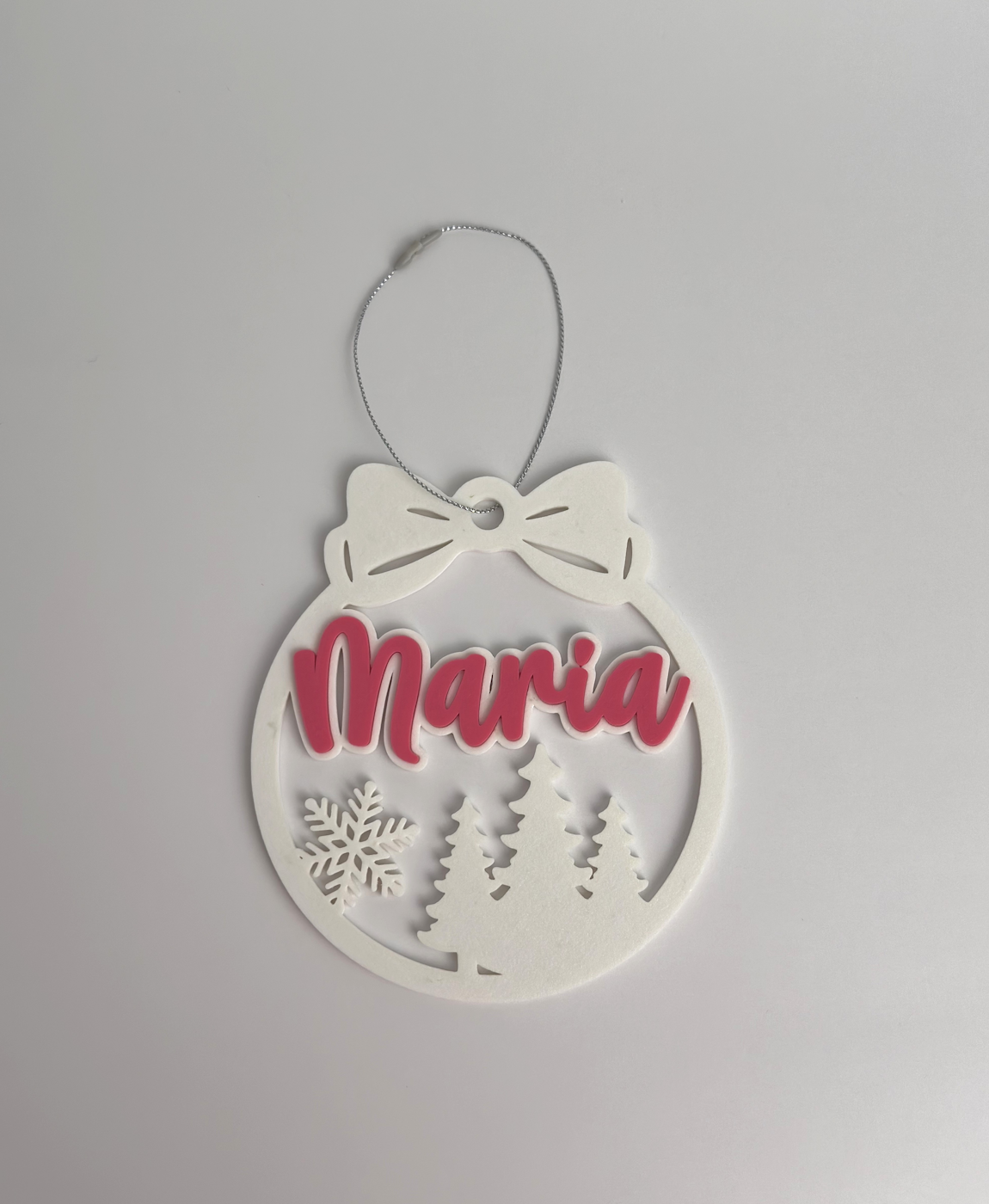 Enfeite de Natal branco com nome 'Maria' em rosa e detalhes de árvores e floco de neve.