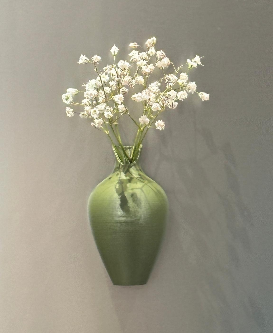 Vaso verde com flores brancas pendurado na parede cinza