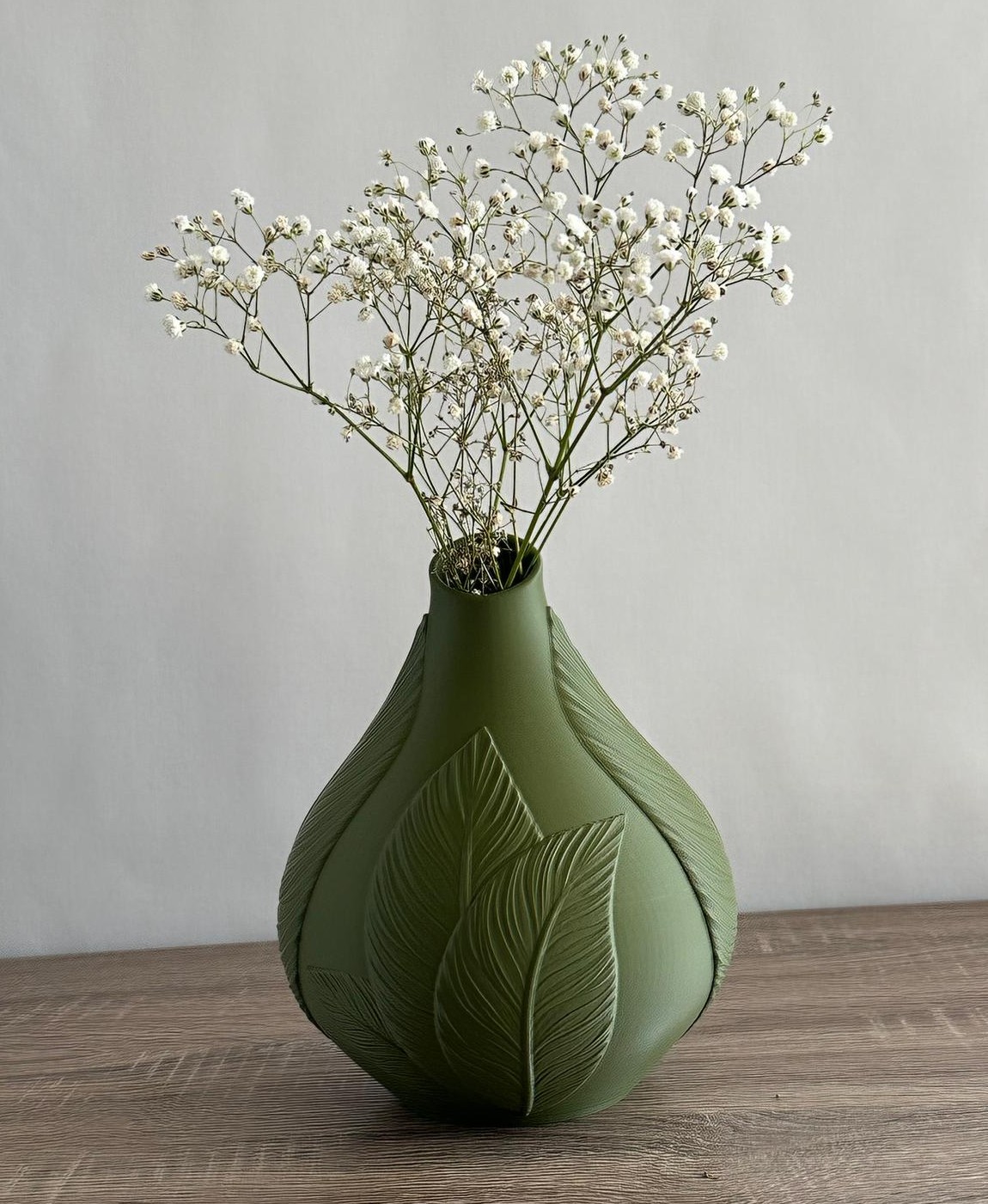 Vaso verde fosco com relevo de folhas e flores brancas finas