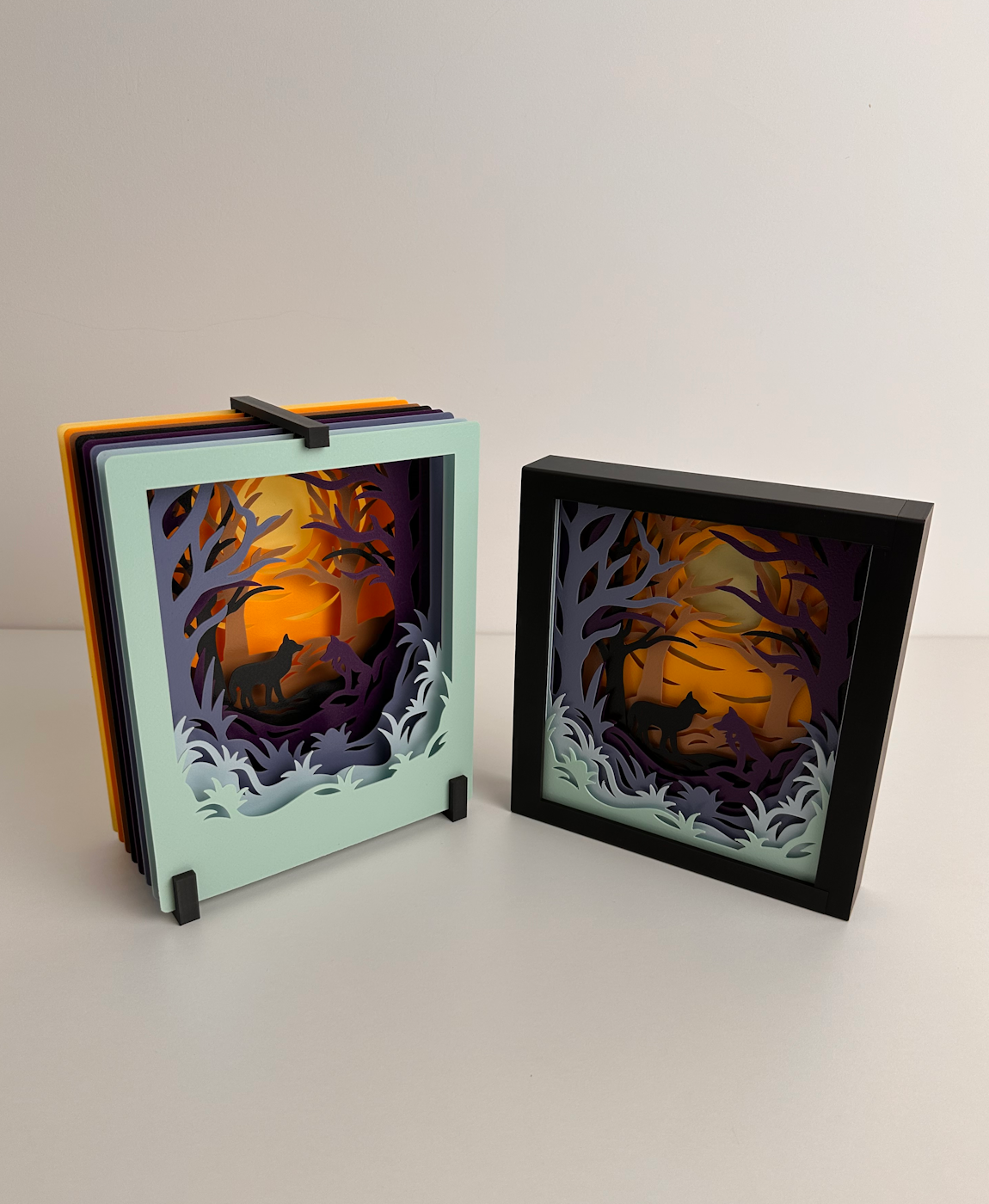 Dois quadros de papel recortado com cena de floresta e lobo.
