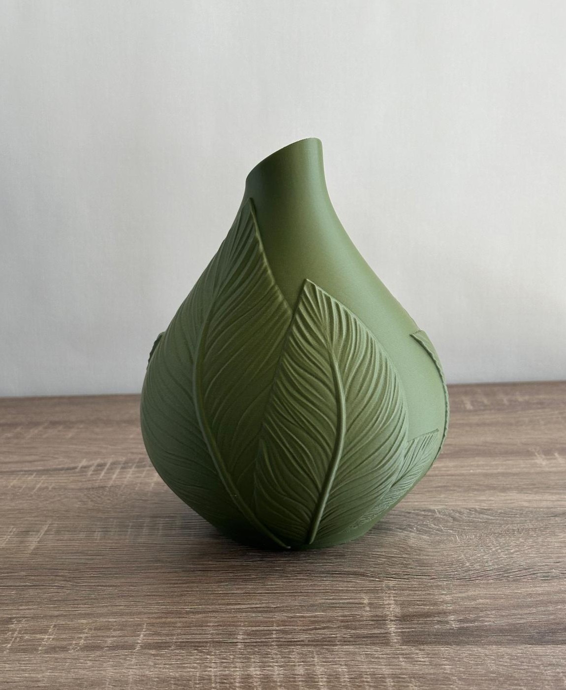 Vaso verde com padrão de folhas em relevo sobre mesa de madeira