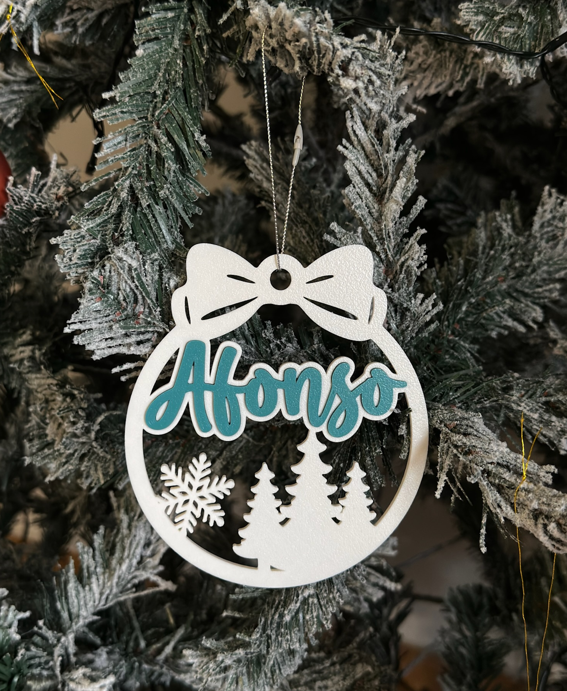 Enfeite de Natal branco e azul com nome 'Afonso' pendurado em árvore de Natal